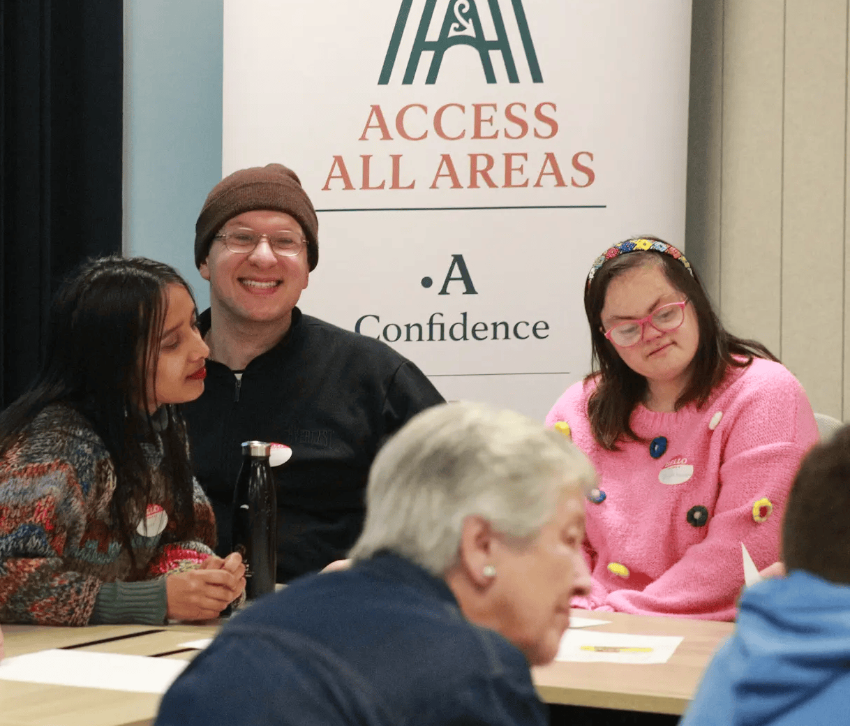 Sean Prenter sitting and smiling alongside two Access Lab participants in front of the Access All Areas banner.