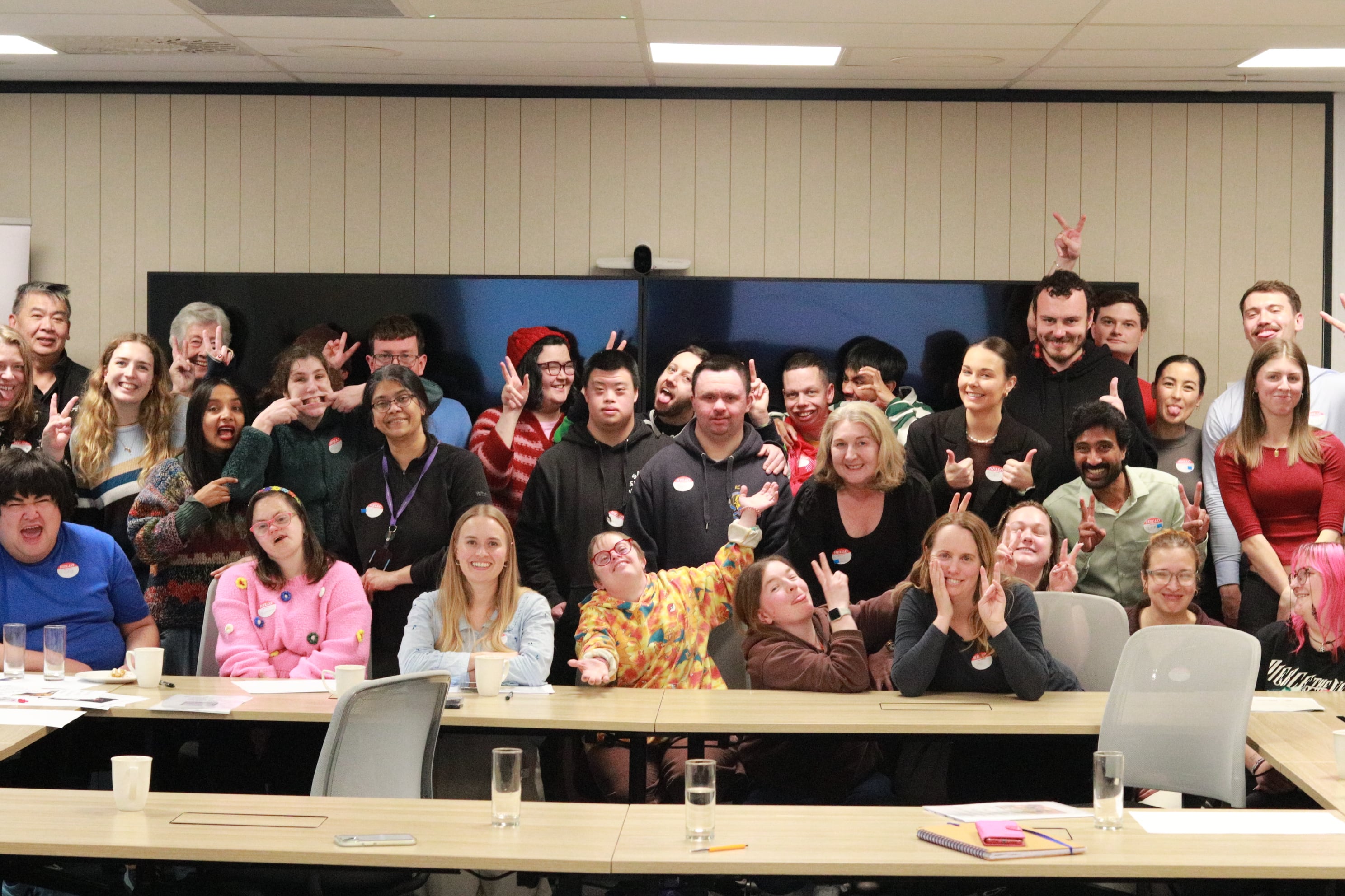 A large group of Access Lab participants, volunteers, and mentors smiling together around the boardroom table.