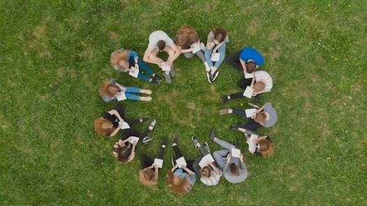 Students seen from a bird's eye view sitting in a circle on grass.